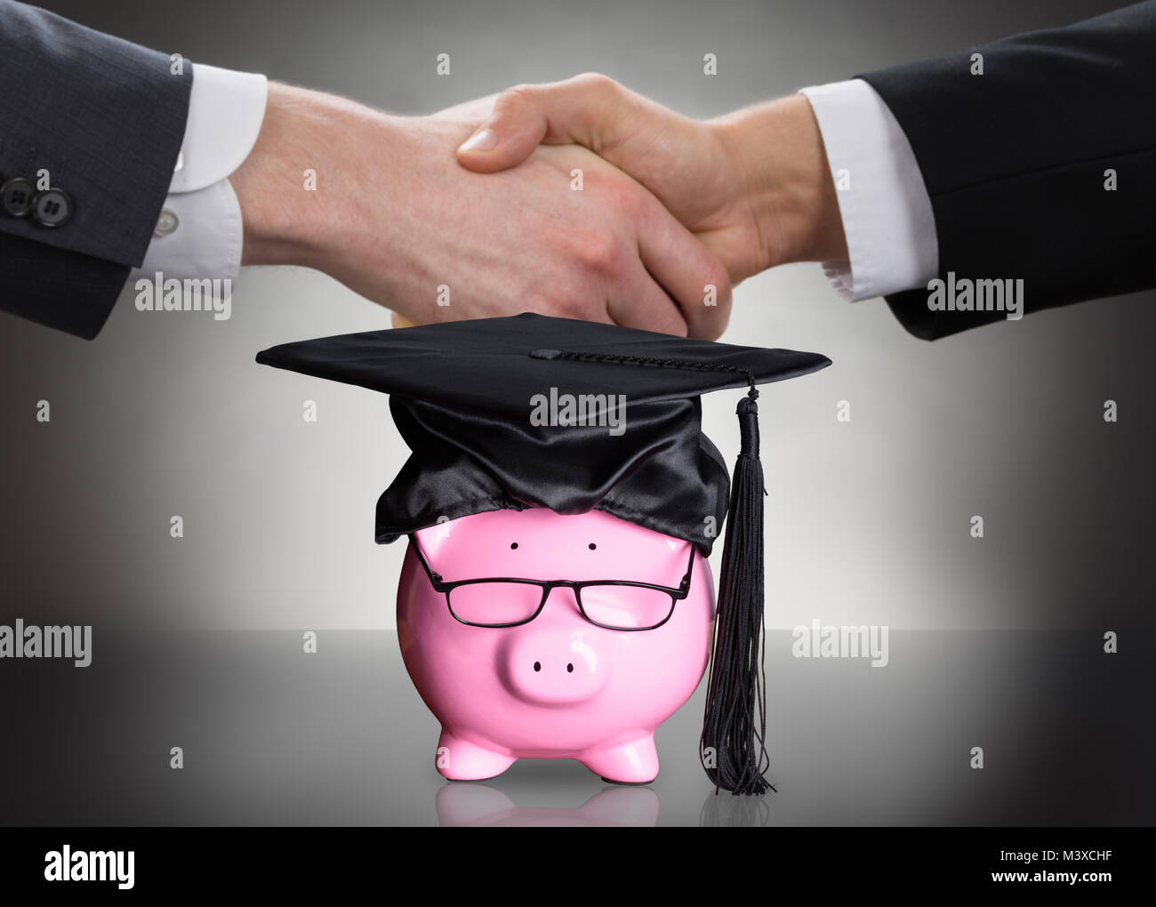 Salvadanaio con graduazione nera cappello e occhiali di fronte a due persone che stringono le mani Foto Stock
