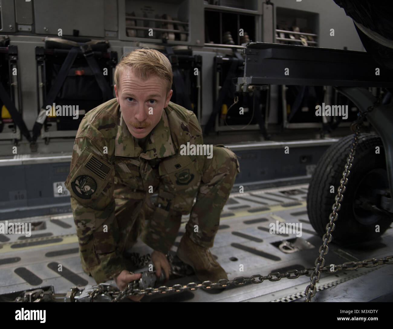 Un U.S. Air Force loadmaster, assegnato alla 816th Airlift Expeditionary Squadron, stringe il movimento delle catene di limitazione su un pezzo di un carico durante le operazioni di caricamento in corrispondenza di Bagram Air Field, Afghanistan, Gennaio 30, 2018. C-17 loadmasters garantire cargo è sicuro e trasportate in modo sicuro e sono responsabili di garantire la rapida erogazione strategica di truppe e di tutti i tipi di carico. (U.S. Air Force Foto di Tech. Sgt. Gregorio Brook) Foto Stock