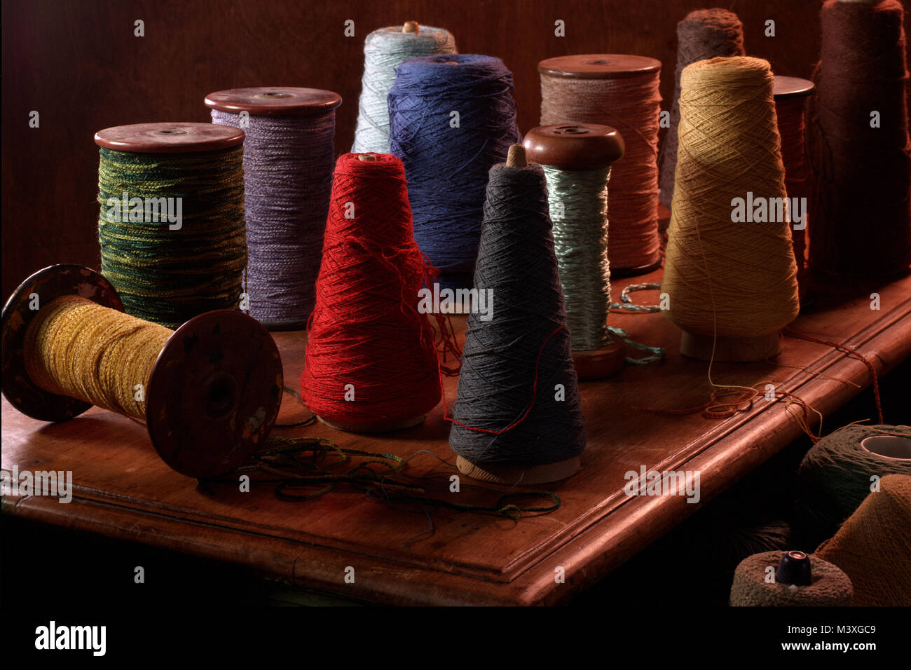 Più steli di tessitura con cotone o lana thread su di essi. Colore verticale fotografia scattata in un studio impostazione con illuminazione drammatica. Terriccio scuro Foto Stock