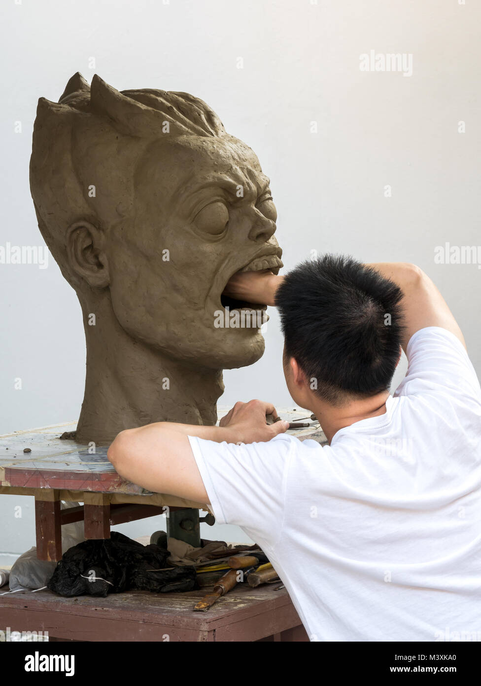 Scultore lavorando sulla sua scultura in argilla, un grande ritratto,con sfondo bianco Foto Stock