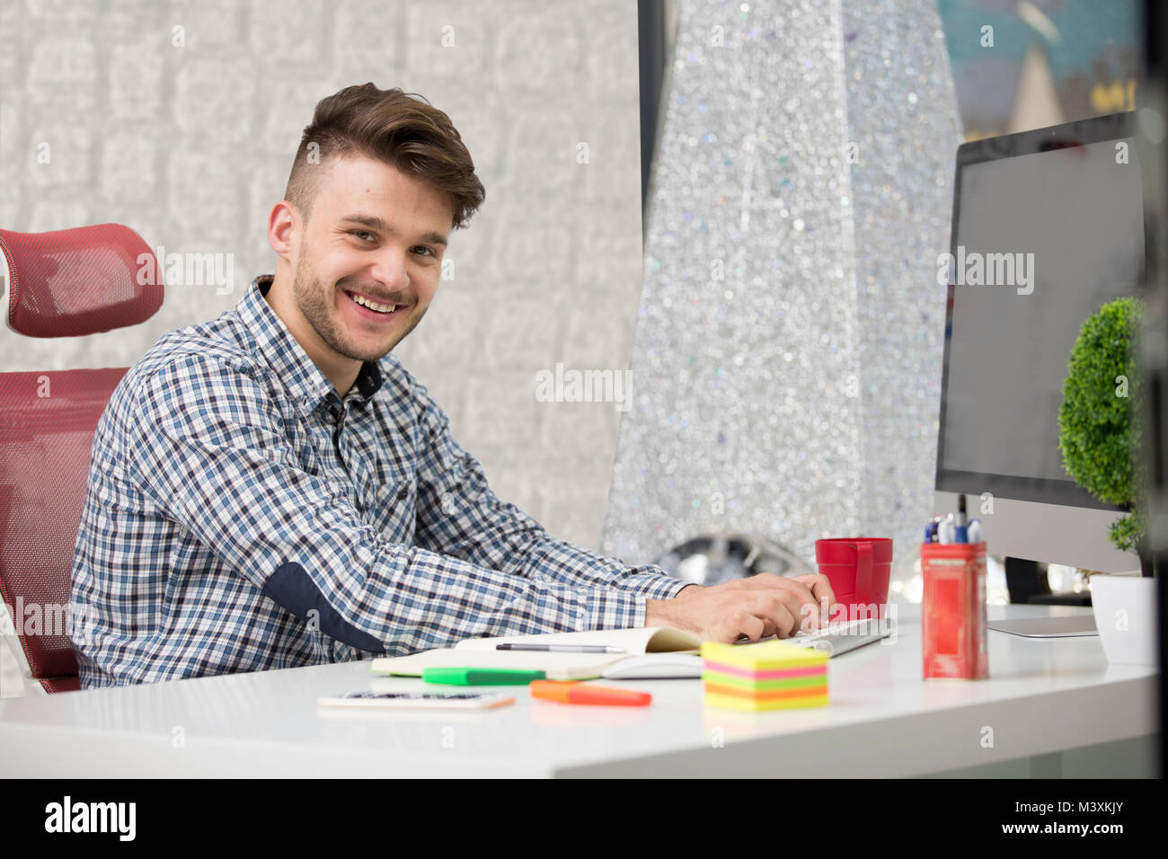 L'uomo prendendo appunti giù dal suo nuovo computer portatile al lavoro in ufficio al mattino con caffè Foto Stock