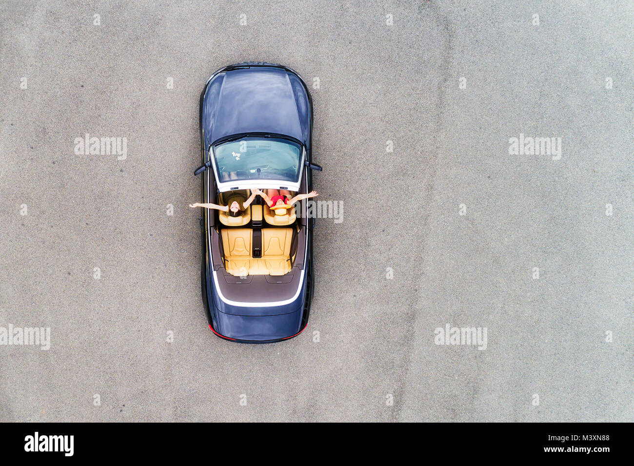 Piccolo sport passeggero autovettura convertibile con soft top down e felice coppia di giovani donne godendo di uno stile di vita e libertà di antenna in vista dall'alto in basso. Foto Stock