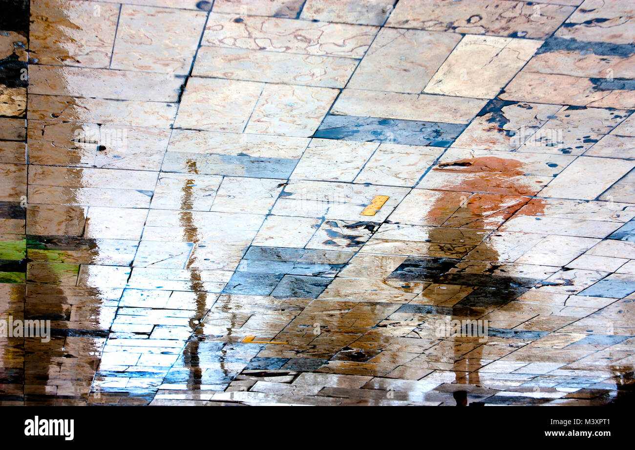 Sfocata Rainy day, una donna in piedi sotto ombrellone rosso silhouette di riflessione sul bagnato city square in alto contrasto Foto Stock