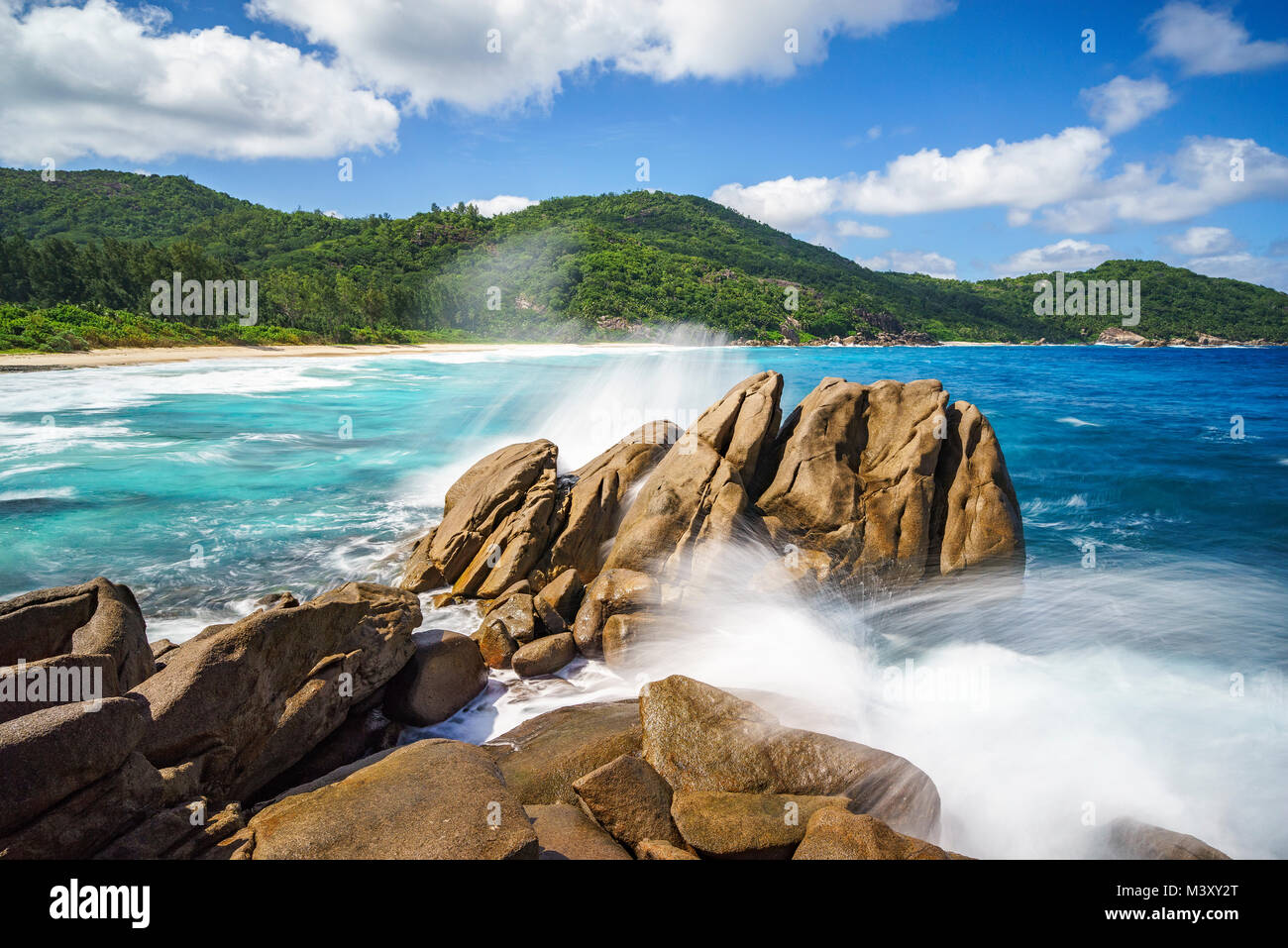 Gli spruzzi di acqua withe grandi fontane d'acqua su una selvaggia spiaggia tropicale con rocce granitiche, palme, acqua turchese sabbia bianca e blu del cielo. La polizia ba Foto Stock