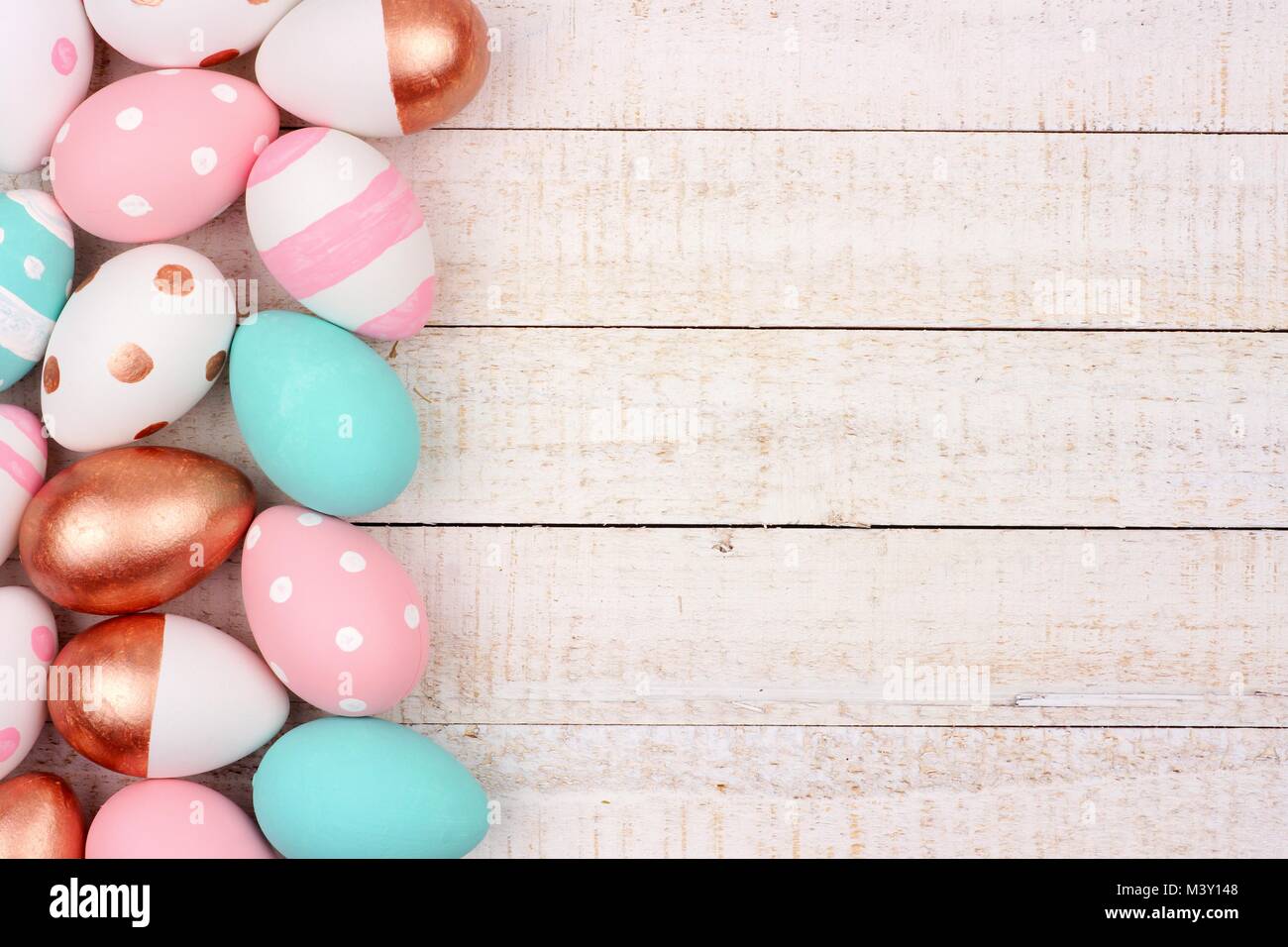 Uovo di Pasqua bordo laterale. Oro rosa, rosa, turchese e di colore bianco su bianco sullo sfondo di legno. Foto Stock