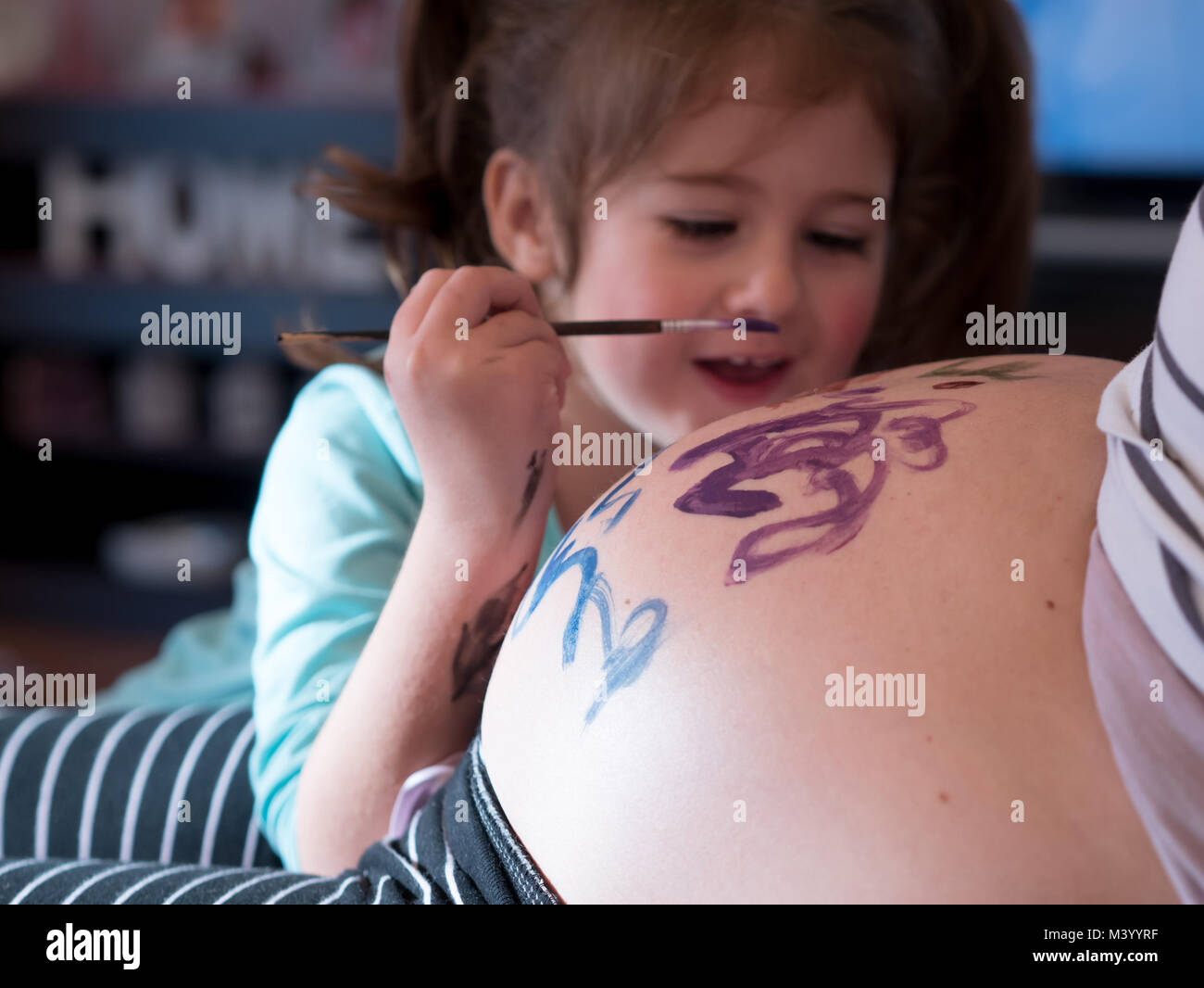 Piccola ragazza pittura madri ventre e sorridente a casa Foto Stock