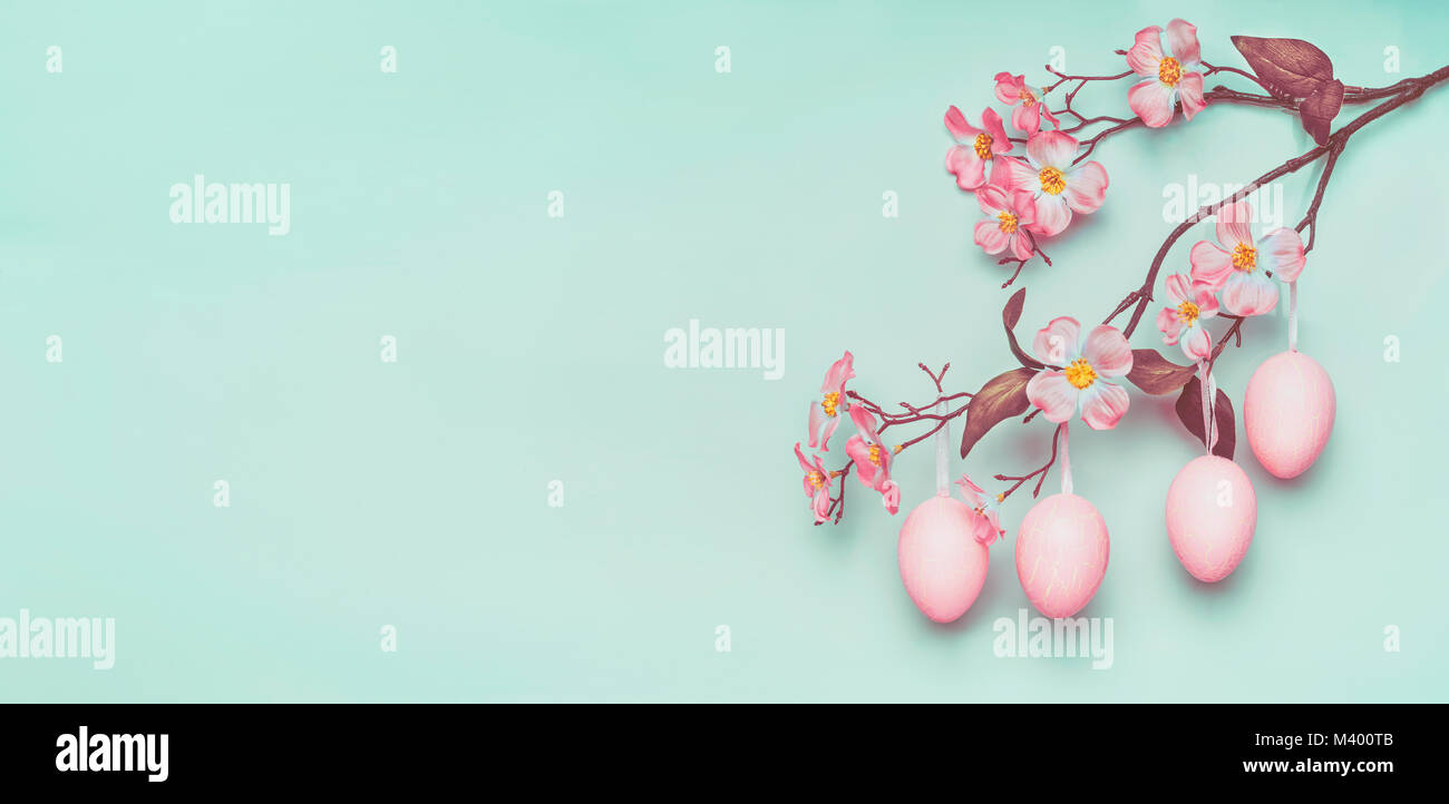 Pasqua confine con appesa rosa pastello uova di Pasqua e la primavera sbocciano i fiori a luce blu a sfondo turchese. Foto Stock