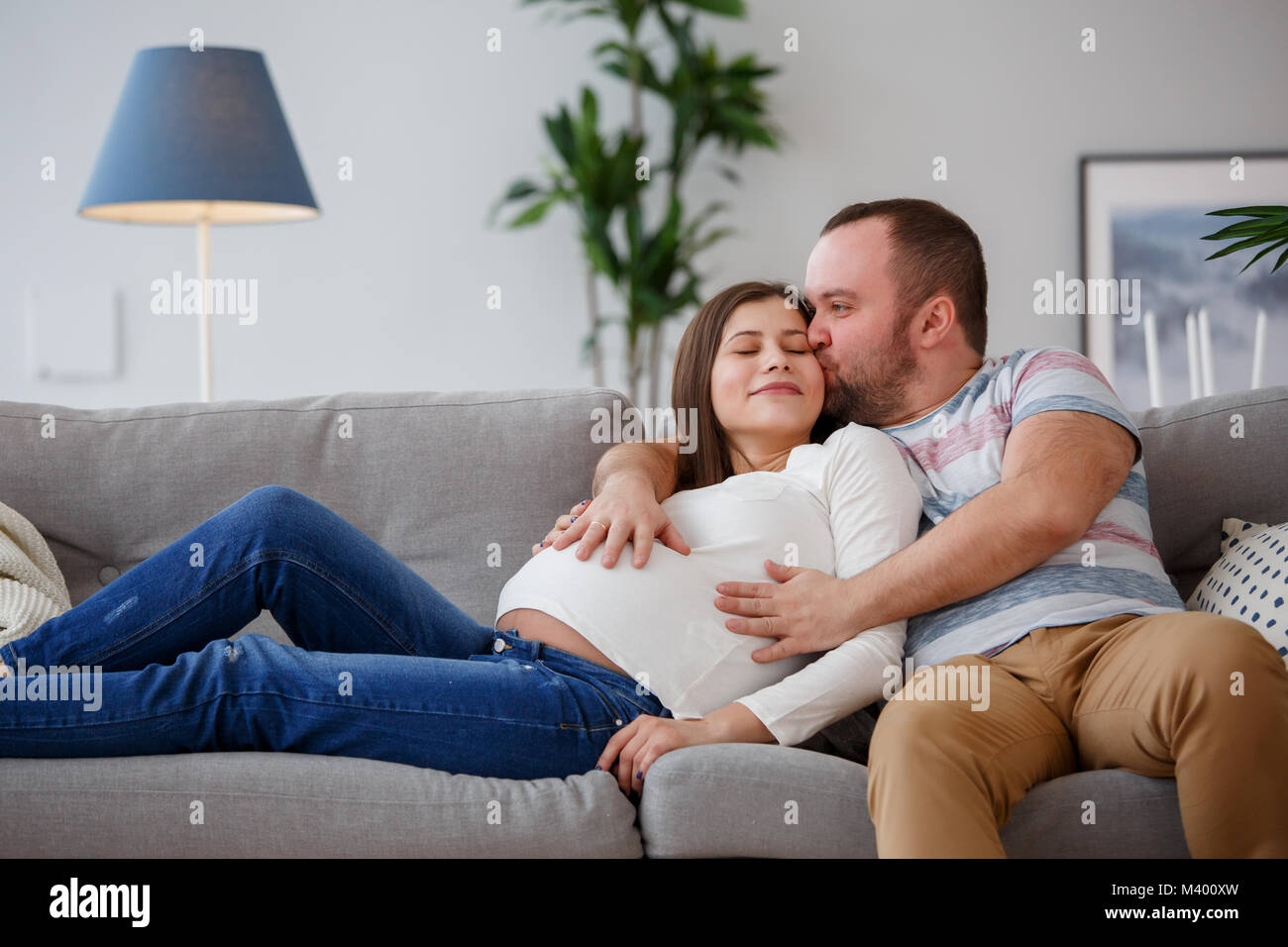 Foto di abbracciando la donna incinta e uomo sul divano grigio Foto Stock