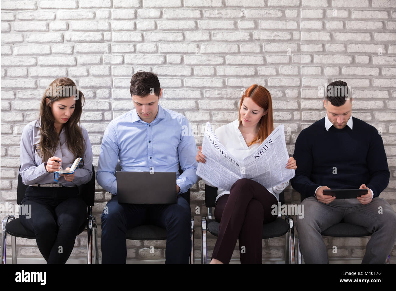 Gruppo di candidati seduti su una sedia in attesa per il colloquio di lavoro contro il bianco muro di mattoni Foto Stock