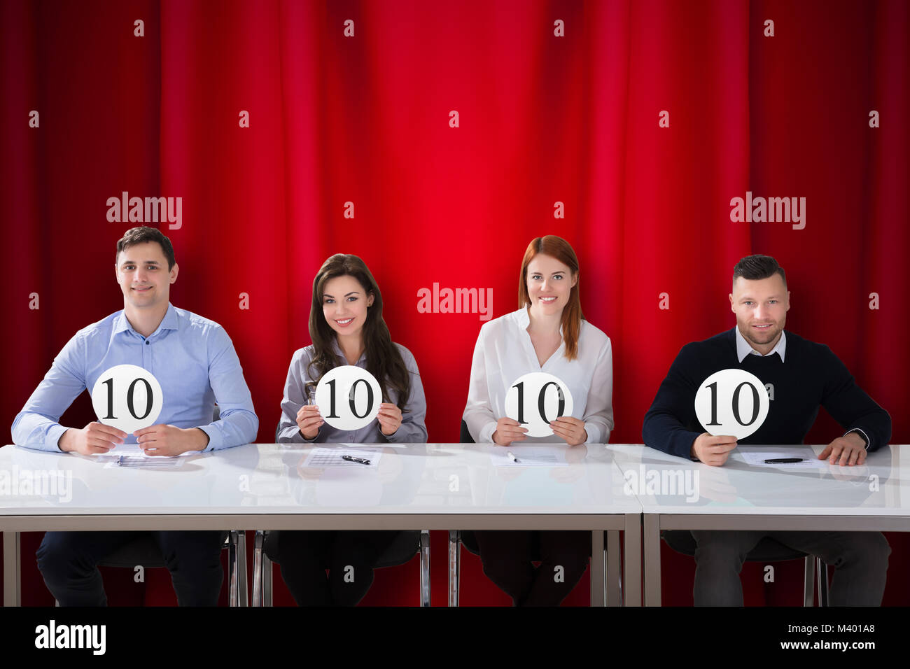 Pannello di felice giudici seduti nella parte anteriore del sipario rosso che mostra il punteggio 10 segni Foto Stock