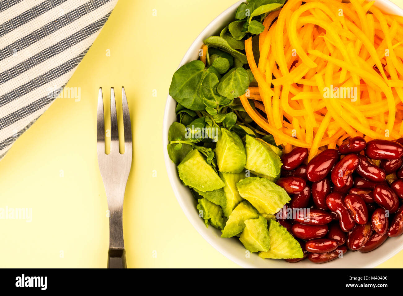 Vegan o cibo vegetariano ciotola con i fagioli borlotti carote di Avocado e insalata di crescione contro un limone o di colore giallo pallido sfondo Foto Stock