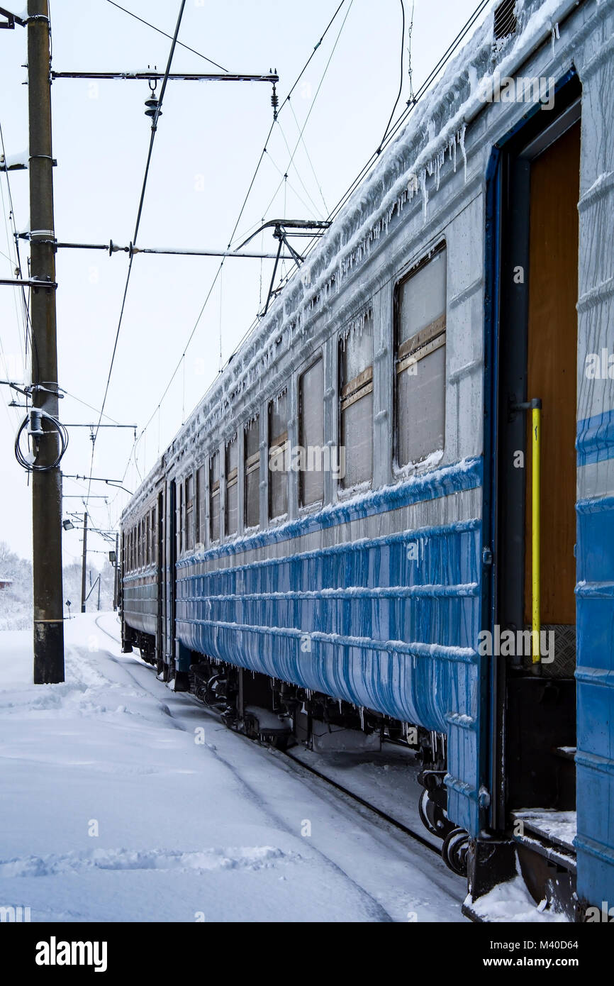 Congelati treno passeggeri con ghiaccioli e ghiaccio sulla sua superficie. Stazione ferroviaria nella fredda stagione invernale Foto Stock