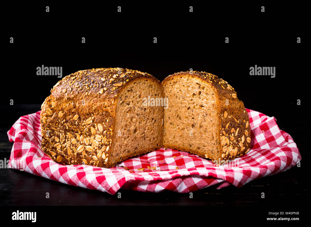 Due metà granaio pane di farro su rosso e bianco asciugamano da cucina e nero lo sfondo di legno. Vista frontale, primo piano. Foto Stock