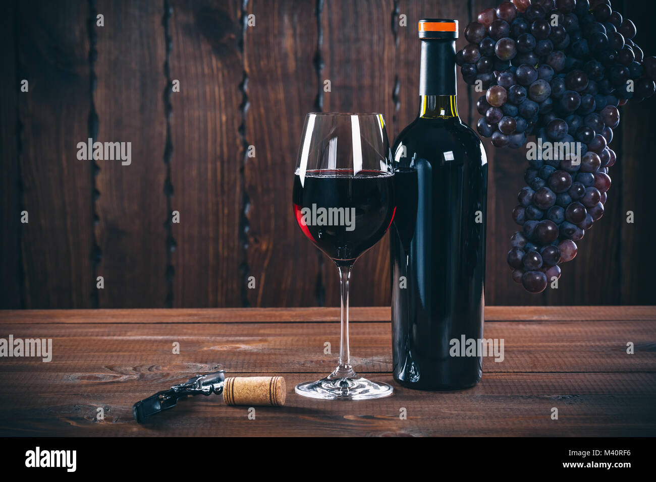 Bottiglia e bicchiere di vino rosso, uva e sughero su sfondo di legno. Foto Stock