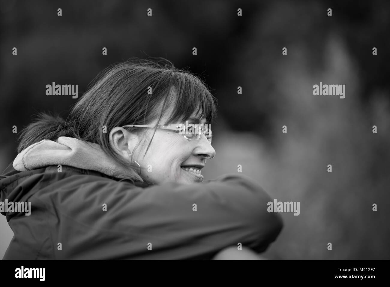 Mono ritratto laterale, donna trendy di 50 anni in occhiali che riposa il mento sulle mani, grande sorriso naturale, sognando l'alba. Consapevolezza, timeout, salute mentale. Foto Stock