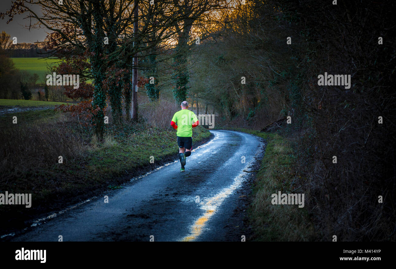 Allenarsi, un uomo che corre una sera d'inverno. Suffolk, Regno Unito. Foto Stock
