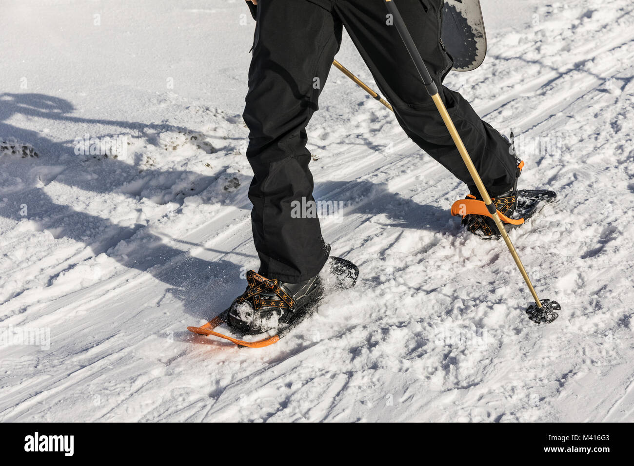 Uomo di colore arancione con le racchette da neve sul percorso di neve. Uomo in racchette da neve con bastoncini da trekking è la neve in montagna. Escursioni con le racchette da neve è più versatile e più alto-p Foto Stock