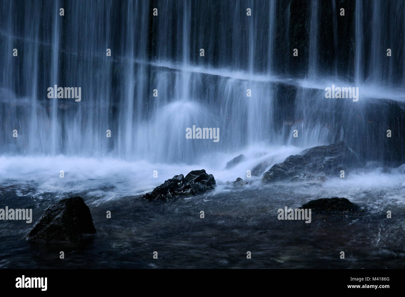 Parzialmente sommerso rocce tra il potente flusso etereo di una cascata. Foto Stock