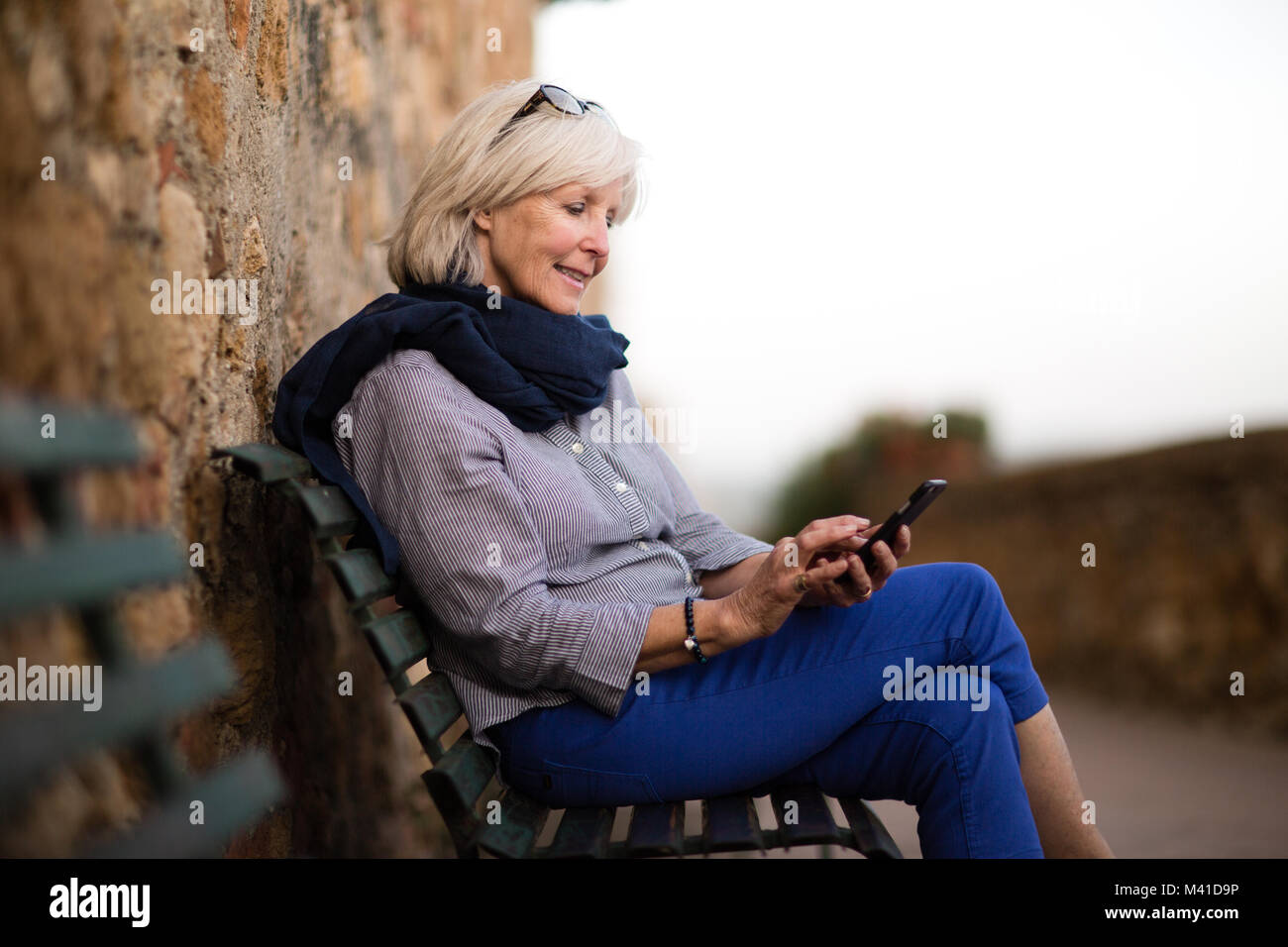 Senior donna relax su un banco di lavoro utilizza lo smartphone Foto Stock