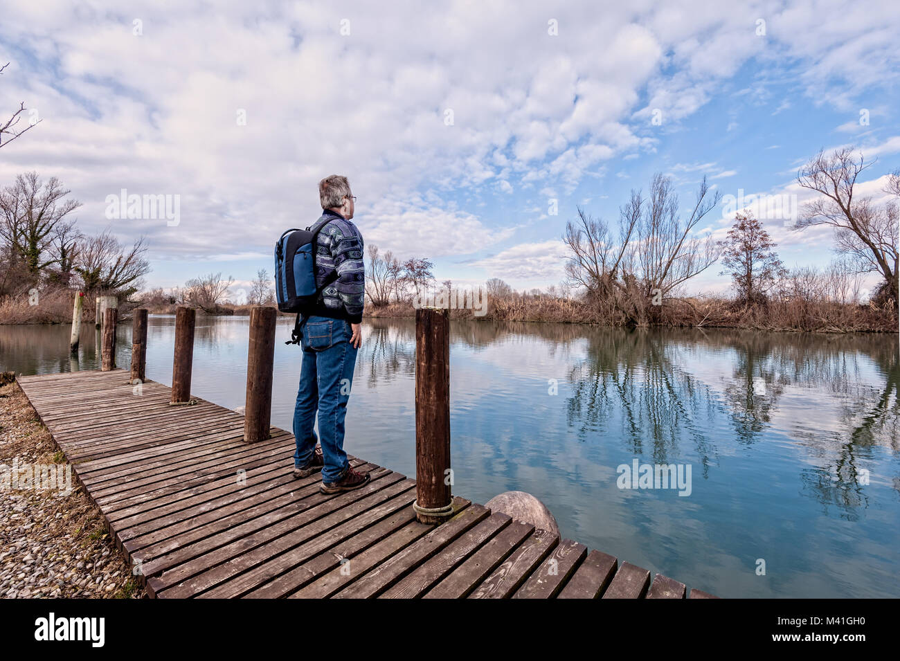 La natura del paesaggio. Escursionista senior con zaino oltre il molo di legno sulla riva del fiume. Foto Stock
