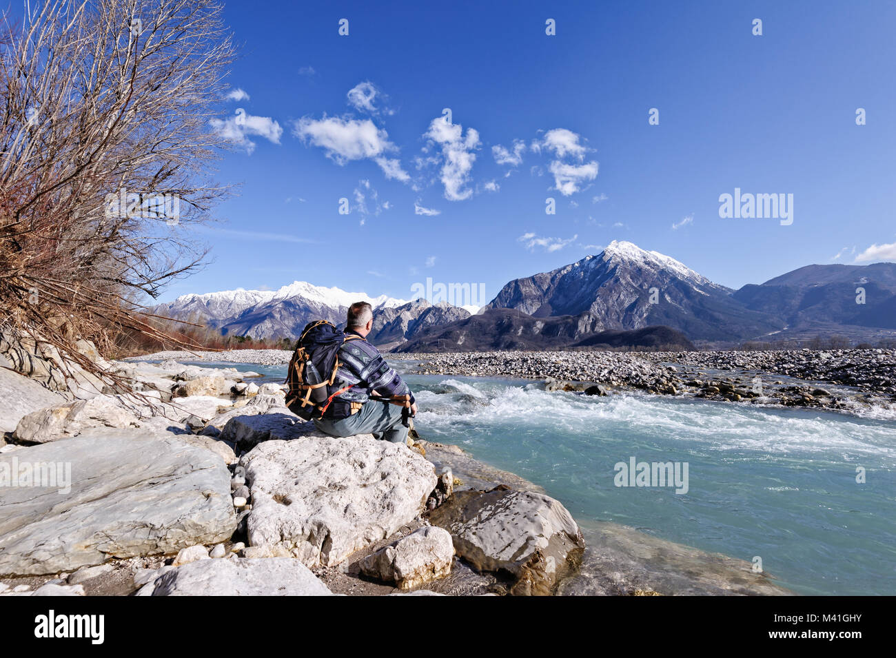 Escursionista seduto sulla riva del fiume sulle rocce, guardando il paesaggio delle montagne.Alpi,l'Italia,Friuli. Foto Stock