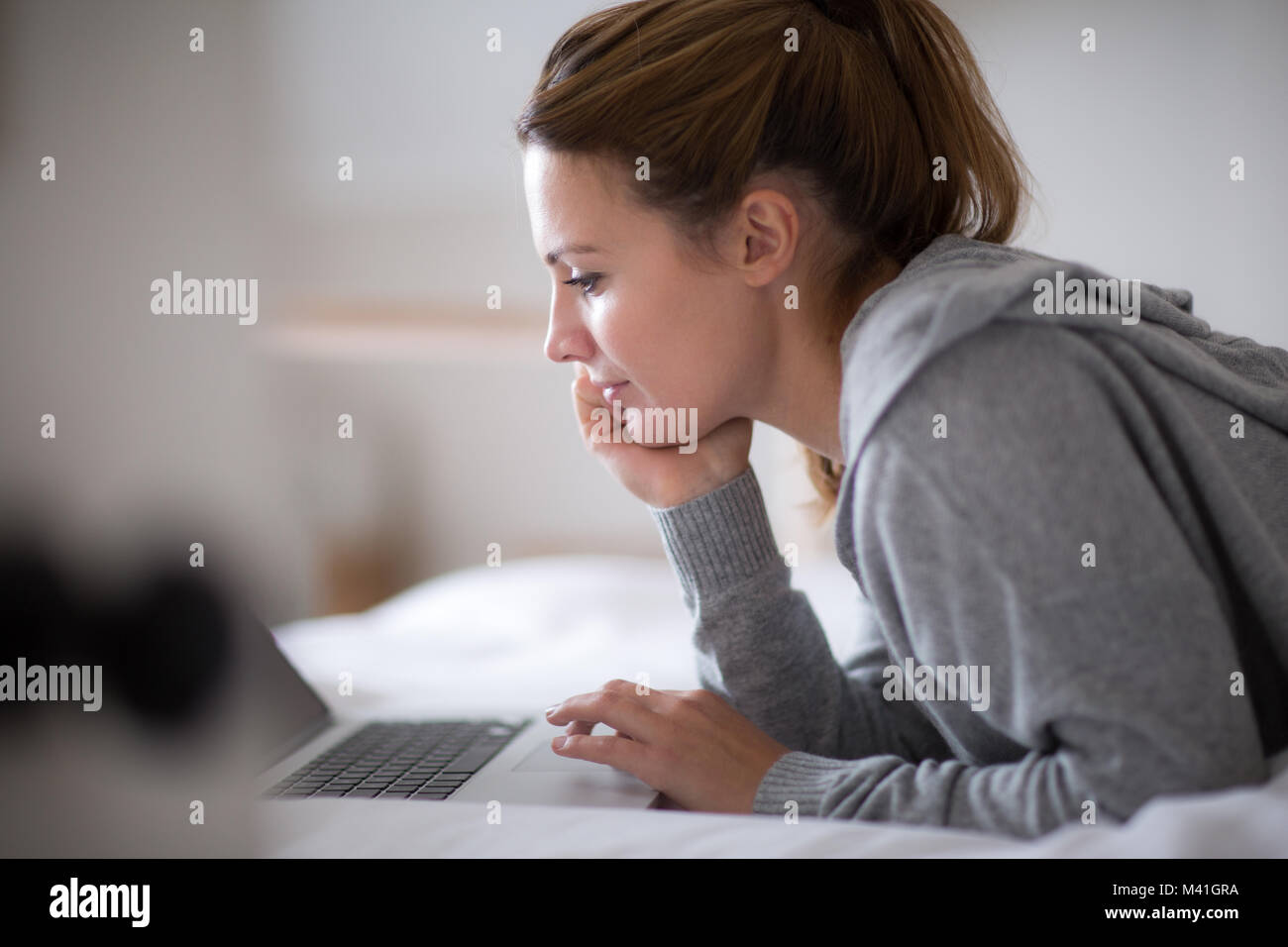 Giovane femmina adulta usando un computer portatile a letto Foto Stock