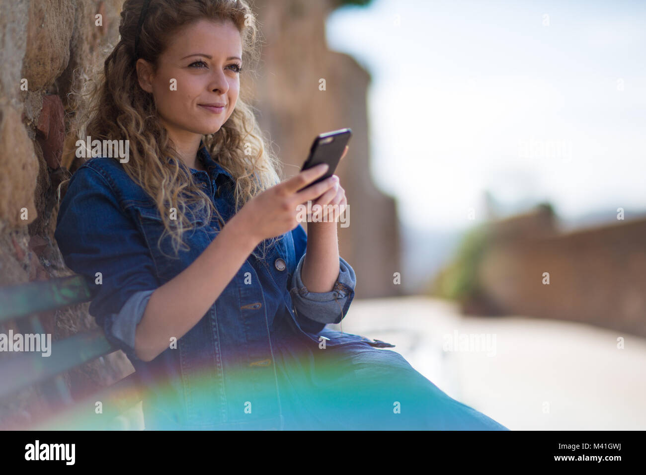 Giovane femmina adulta utilizzando lo smartphone, seduta su una panchina Foto Stock
