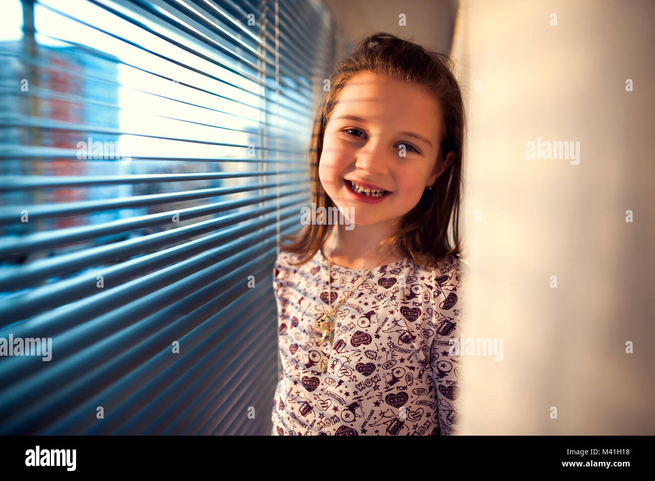 Ragazza sorridente in piedi accanto alla finestra con spranghe Foto Stock