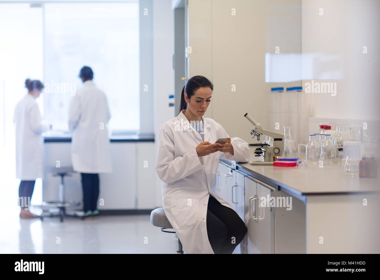 Donna scienziato utilizza lo smartphone in laboratorio Foto Stock
