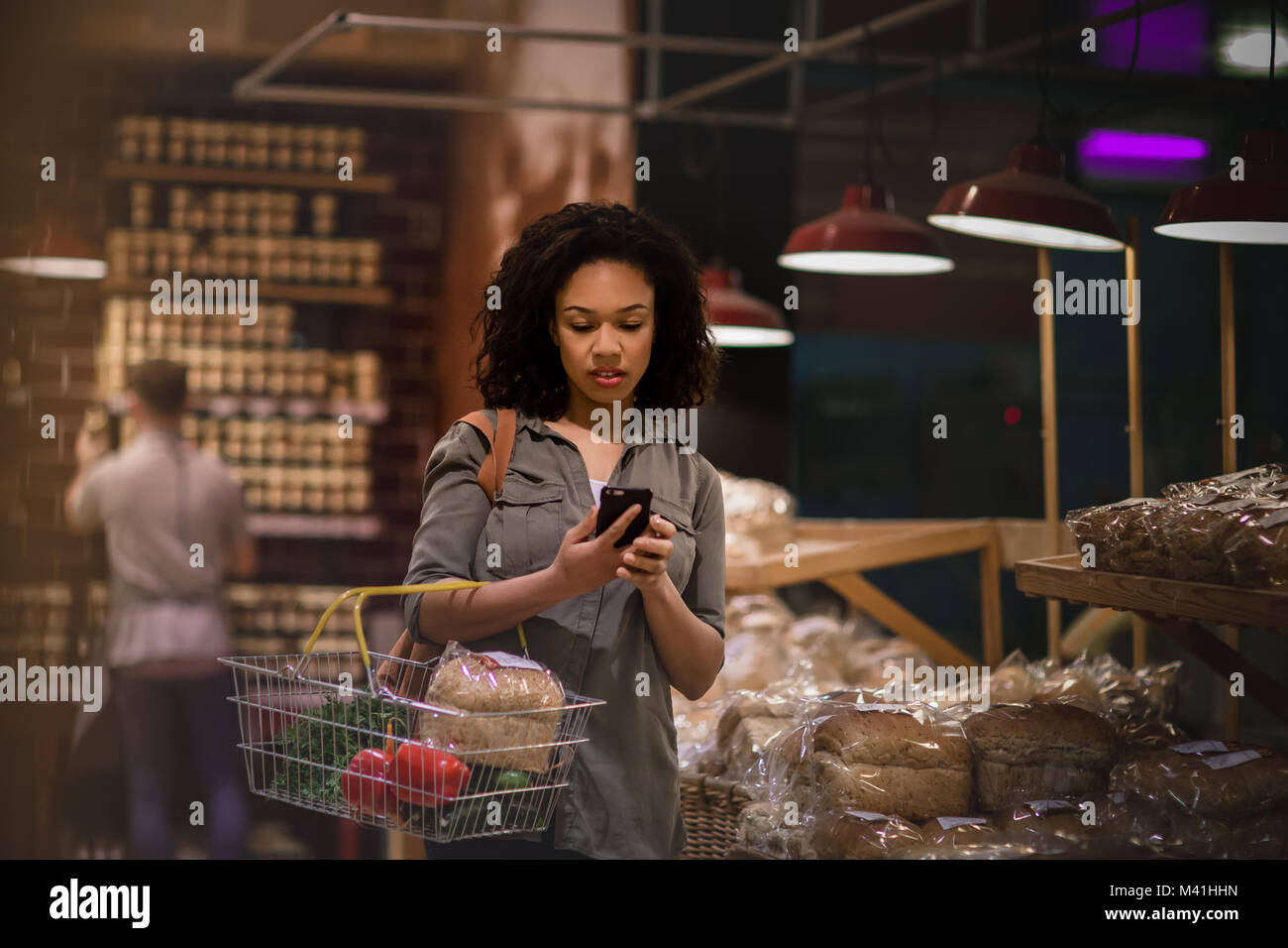La donna a tarda notte negozi di alimentari e utilizza lo smartphone Foto Stock