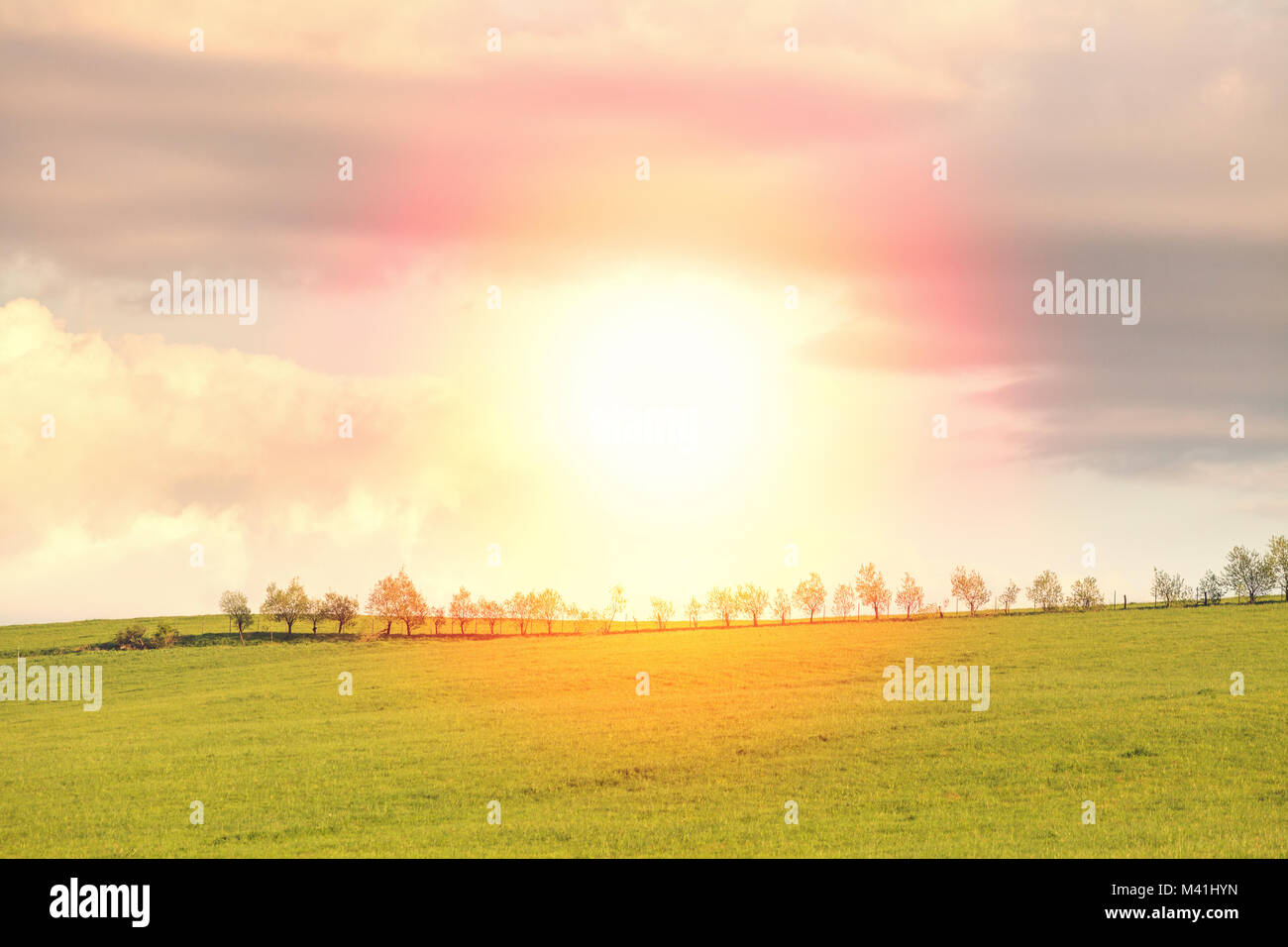 Blu cielo nuvoloso su verdi colline e strade di campagna con il sole che splende direttamente nella fotocamera Foto Stock