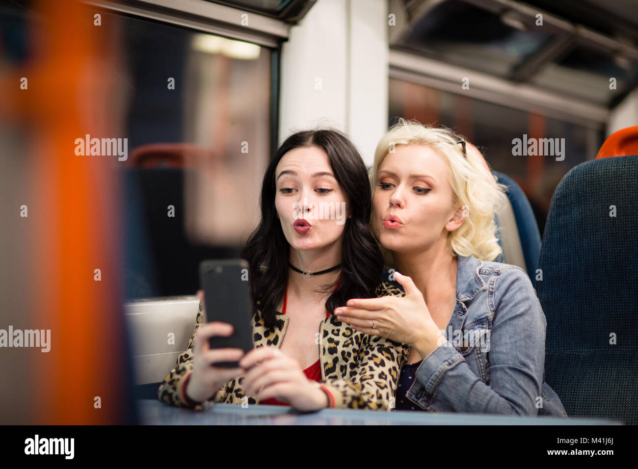 Giovane femmina adulta di amici in viaggio su un treno notturno tenendo selfie Foto Stock