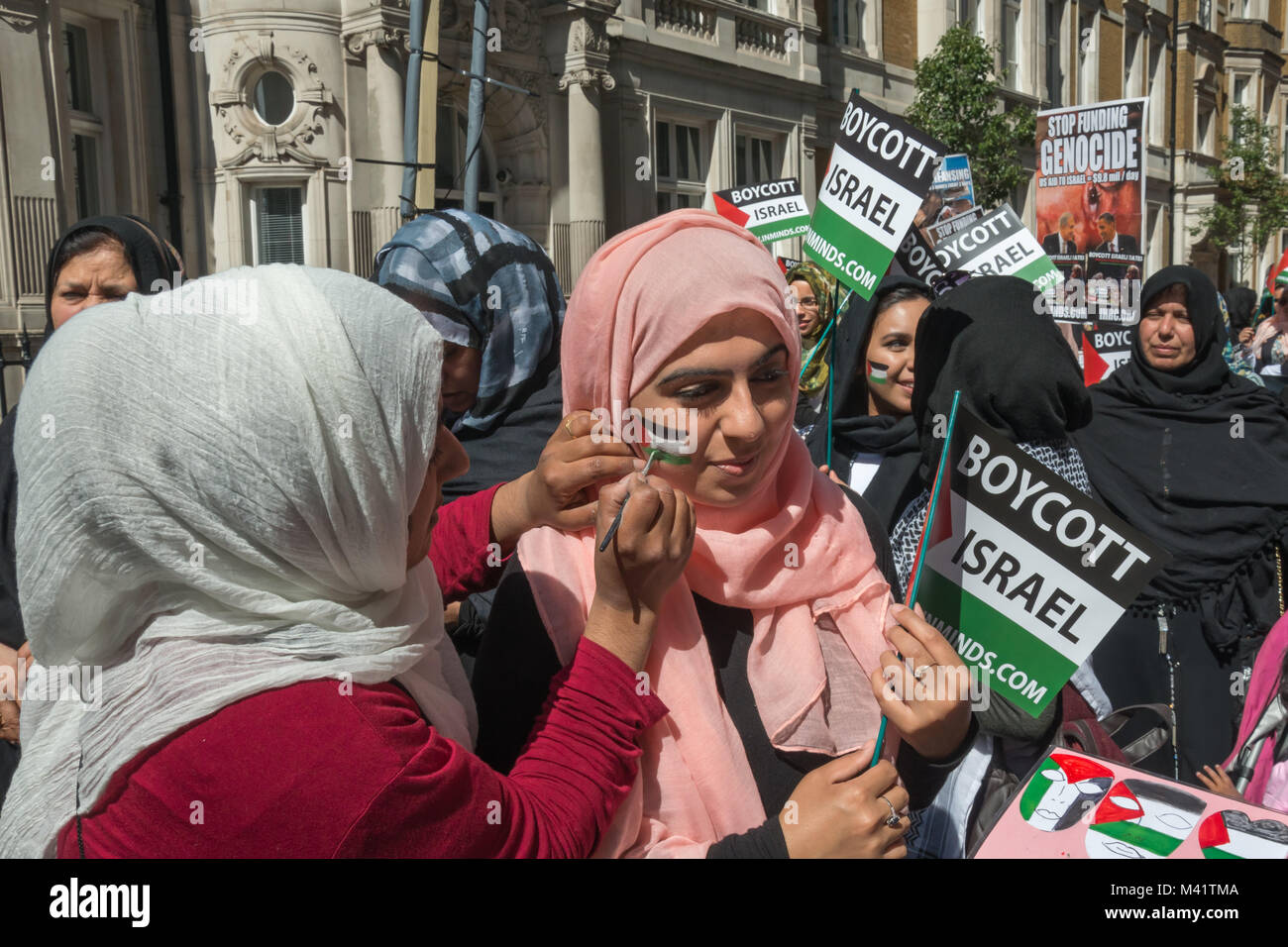 Una donna mette la rifinitura di un palestinese flage ha dipinto sulla guancia di un'altra donna all'inizio di Al Quds giorno marzo a Londra. Foto Stock