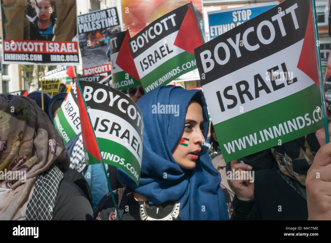 Una donna in un velo di colore blu con una bandiera palestinese dipinta sulla sua guancia è circondato da "Boicottare Israele" bandiere palestinese come ella attende all'inizio di Al Quds giorno marzo a Londra. Foto Stock