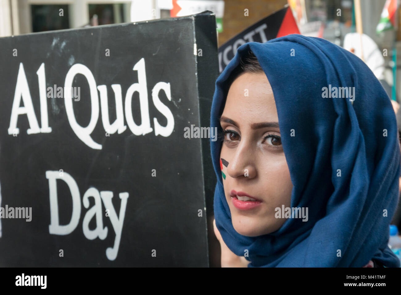 Una donna in un velo di colore blu con una bandiera palestinese dipinta sulla sua guancia contiene una grande scheda con un messaggio su Al Quds giorno. Foto Stock
