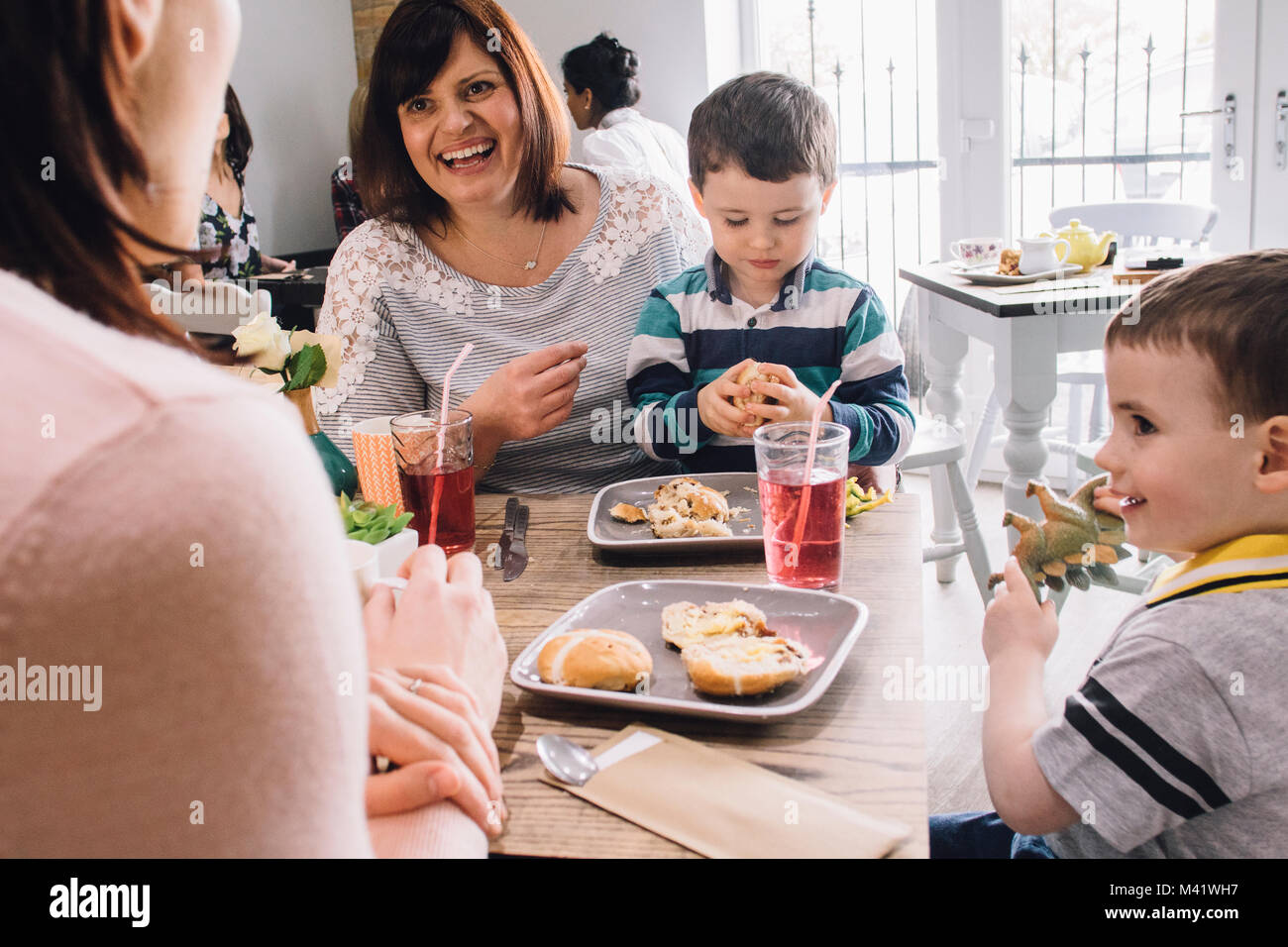 Due donne sono socializzare su di tè e biscotti. Una delle donne ha due figli e stanno giocando con le focaccine e dinosauri giocattolo. Foto Stock