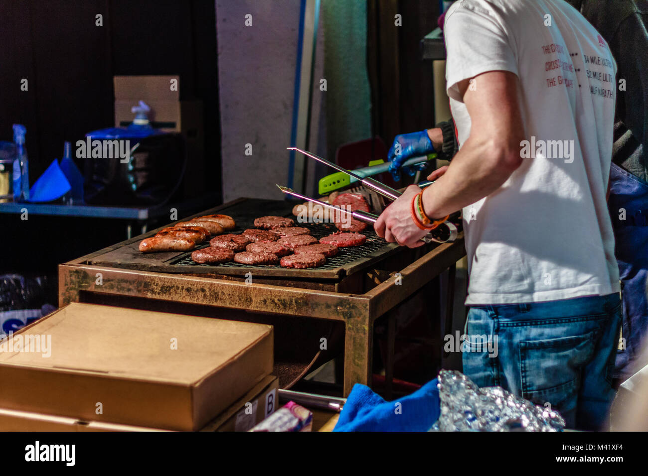 Uomo in bianco t shirt hamburger di cottura sulla griglia in corrispondenza di un festival di strada. Gennaio wassail, Stoke Gabriel, Devon, Regno Unito. 2018. Foto Stock