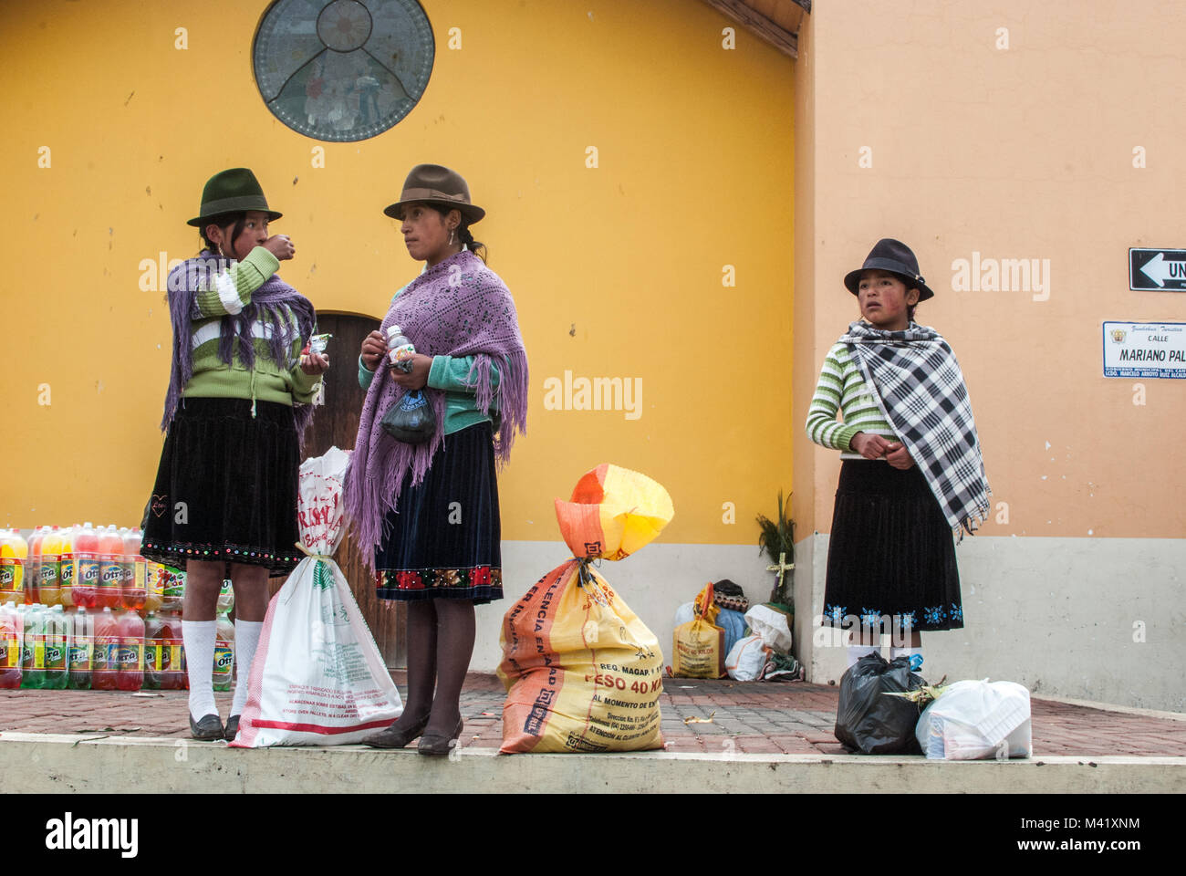 Tre giovani ragazze indigene in piedi indossando vestiti tradizionali con sacchi di produrre in un mercato in Ecuador Foto Stock