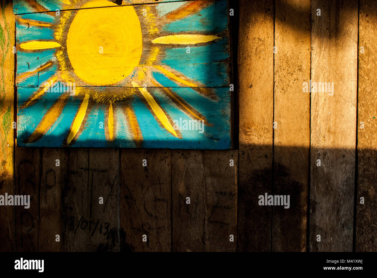 Un semplice bambino-come la pittura di un sole giallo sul lato di una casa in legno illuminato dalla luce solare Foto Stock