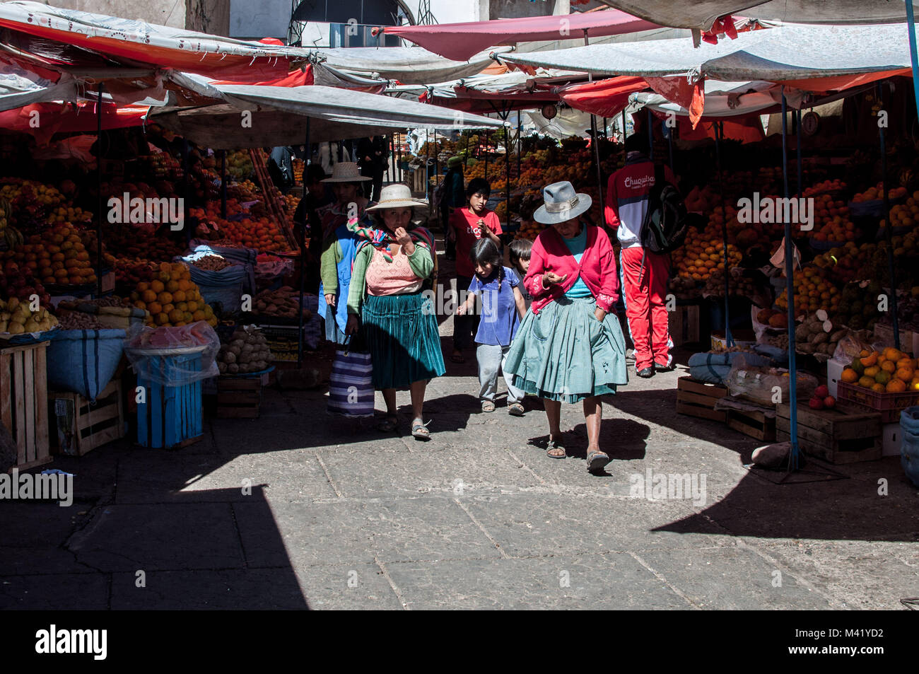 Le donne indigene indossando cappelli tradizionali e abbigliamento a piedi attraverso un mercato con i loro figli in Sucre, Bolivia Foto Stock