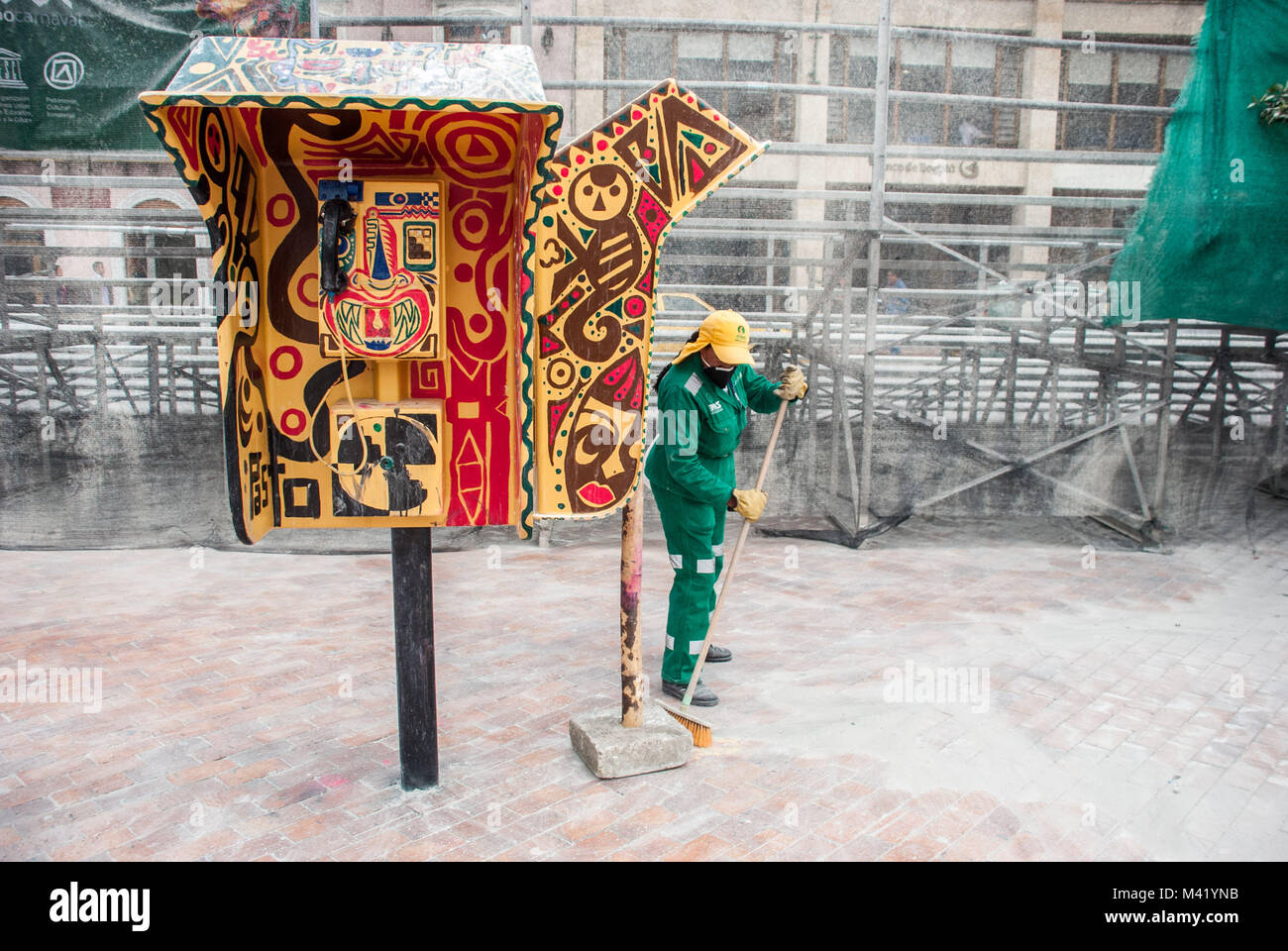 Un pulitore di via spazzare accanto a un decorate luminosamente telefono pubblico dopo un carnevale di Pasto, Colombia Foto Stock