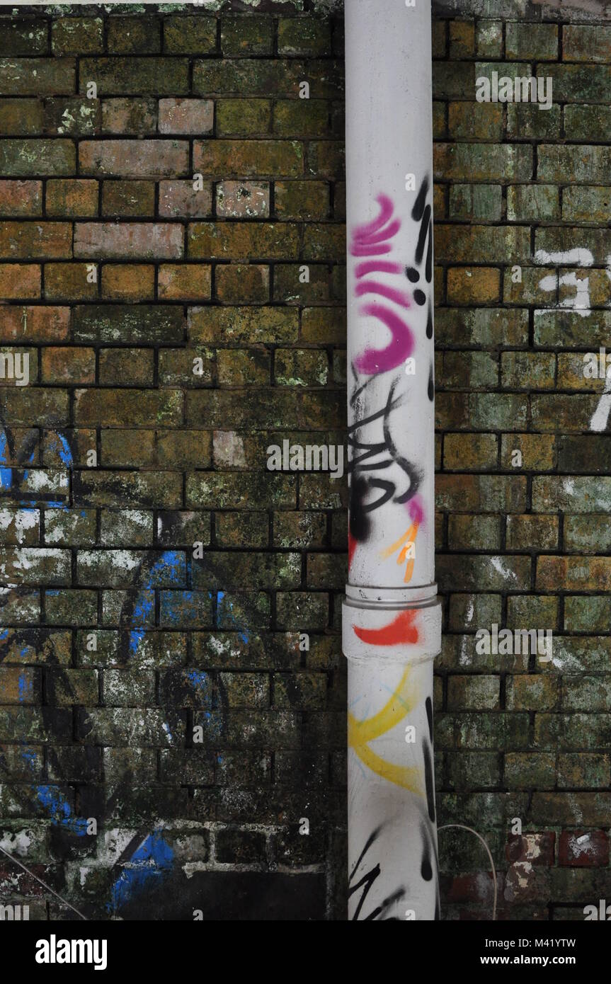 Un graffiti-coperto drainpipe attaccato ad una usura della parete di mattoni in un magazzino Foto Stock