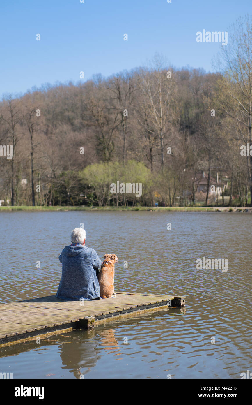 Uomo seduto con il suo cane sul pontile in natura il lago Foto Stock