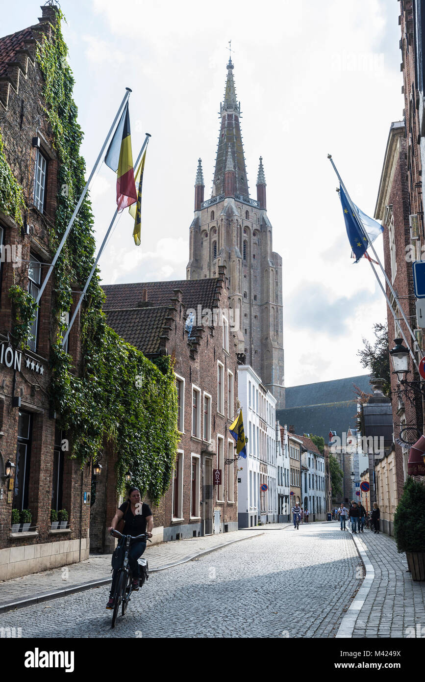 Bruges, Belgio - 1 Settembre 2017: Street con le persone camminare e una donna in bicicletta con il campanile della Madonna in background nel medioevo Foto Stock