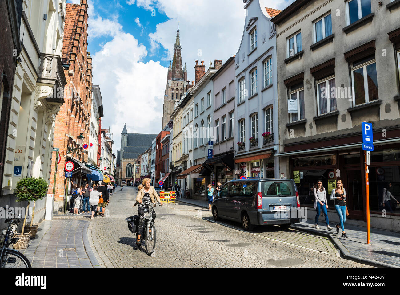 Bruges, Belgio - 1 Settembre 2017: Street con le persone camminare e una donna in bicicletta con il campanile della Madonna in background nel medioevo Foto Stock