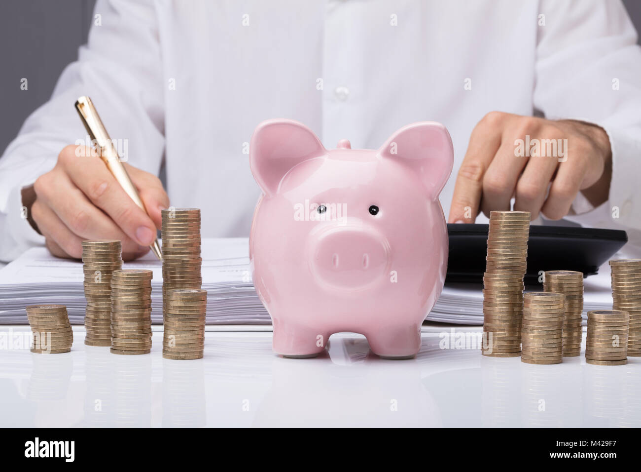 Close-up di imprenditore il calcolo di Bill con Piggybank e monete impilate sulla scrivania in ufficio Foto Stock