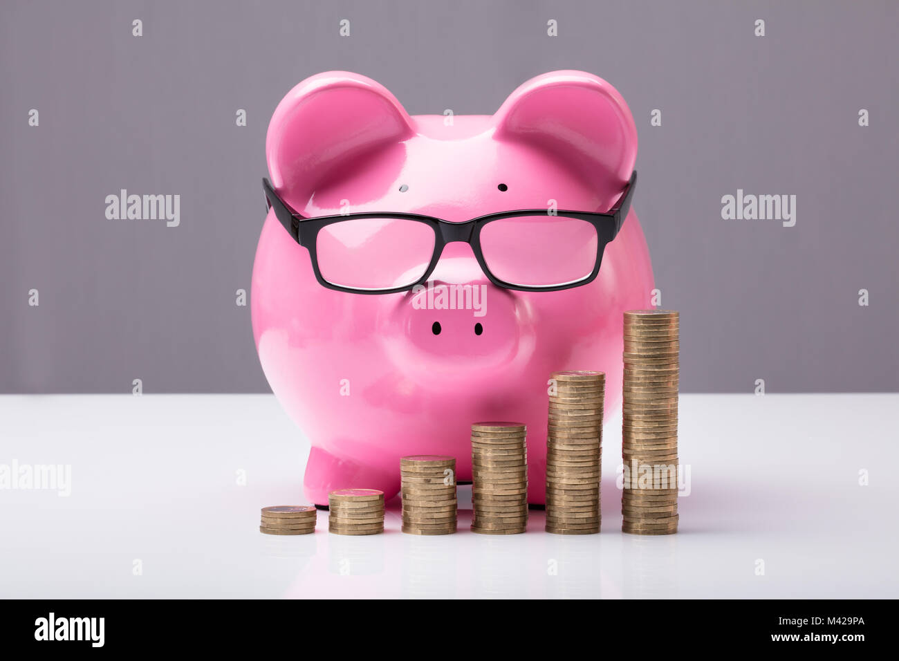 Close-up di Piggybank e monete impilate su scrivania Foto Stock