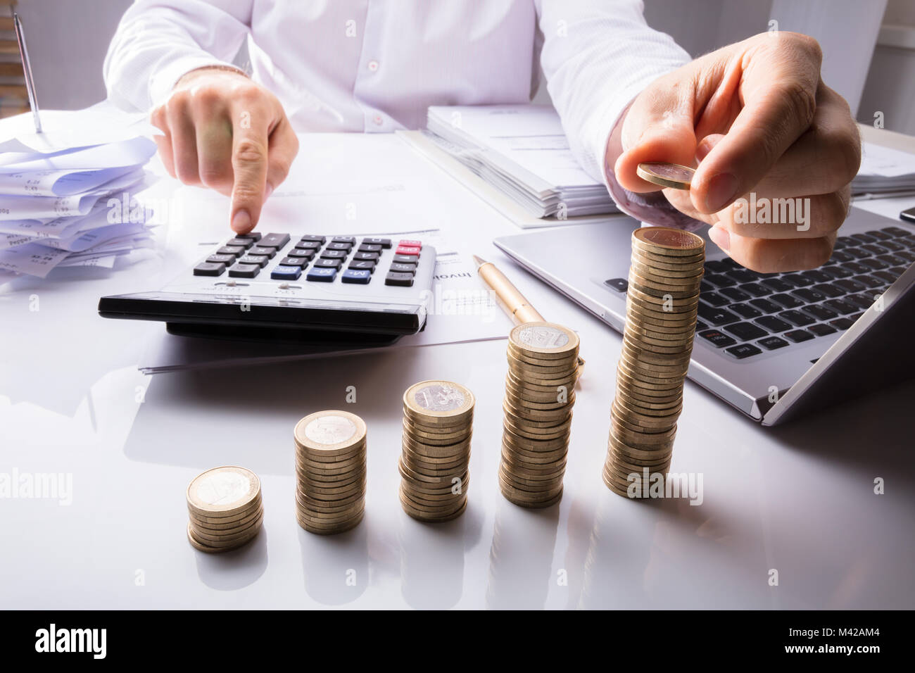 Close-up di una persona d'affari contare monete utilizzando la calcolatrice con Laptop e documenti sulla scrivania Foto Stock