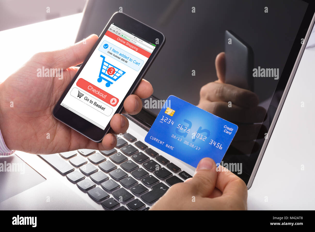 Persona in possesso di Carta di Credito facendo shopping online utilizzando Smart Phone nella parte anteriore del computer portatile Foto Stock