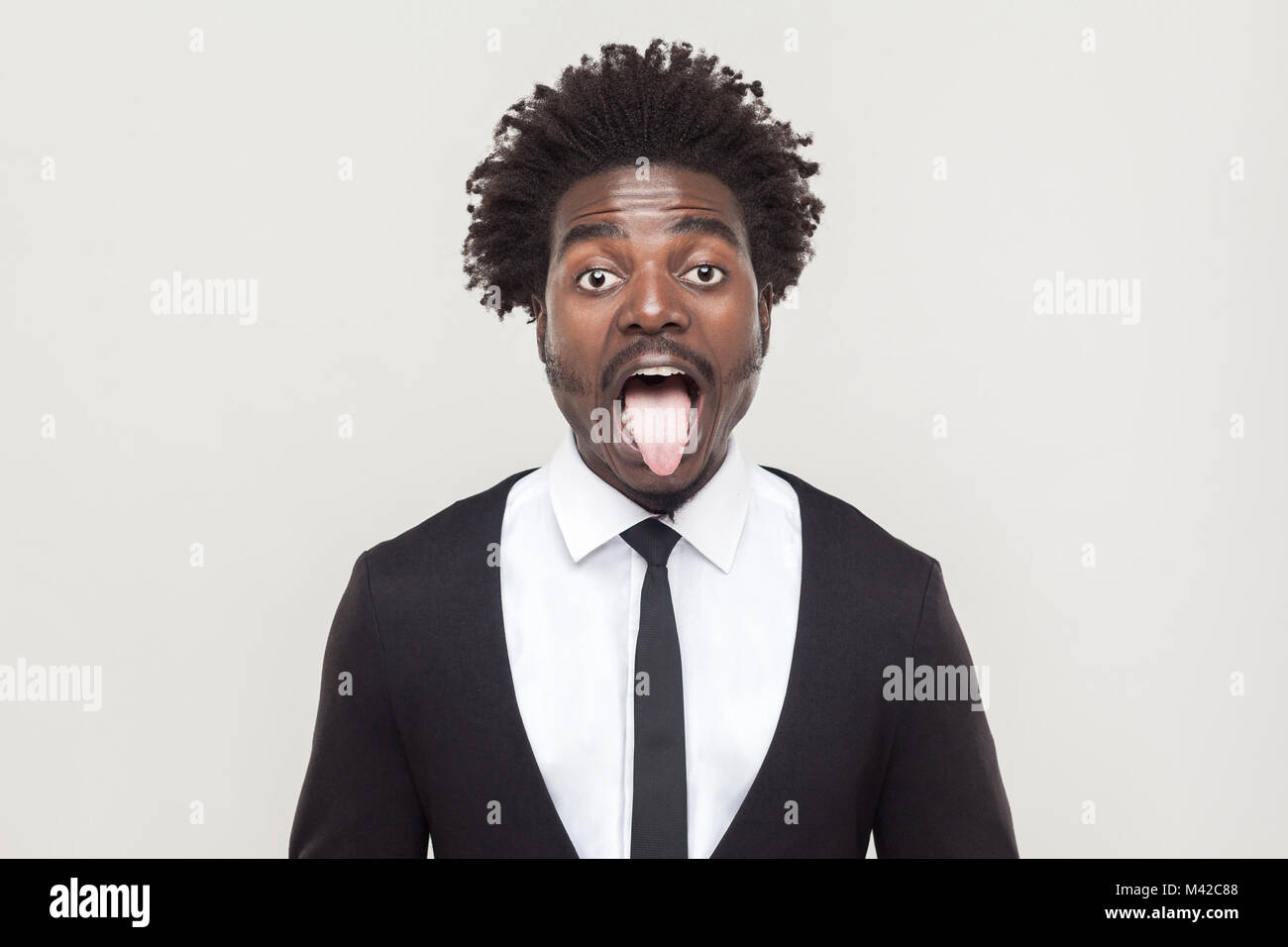 Crazy afro uomo che guarda la fotocamera e la lingua di fuori. Studio shot, sfondo grigio Foto Stock